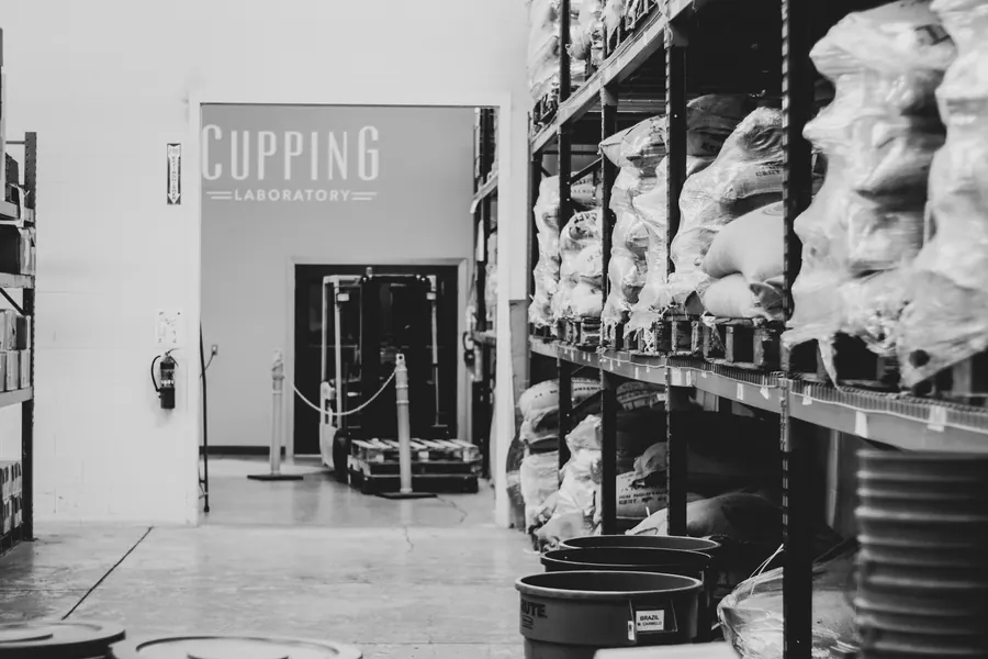 Black-and-white view of coffee sacks on warehouse racks beside a cupping laboratory in Oregon